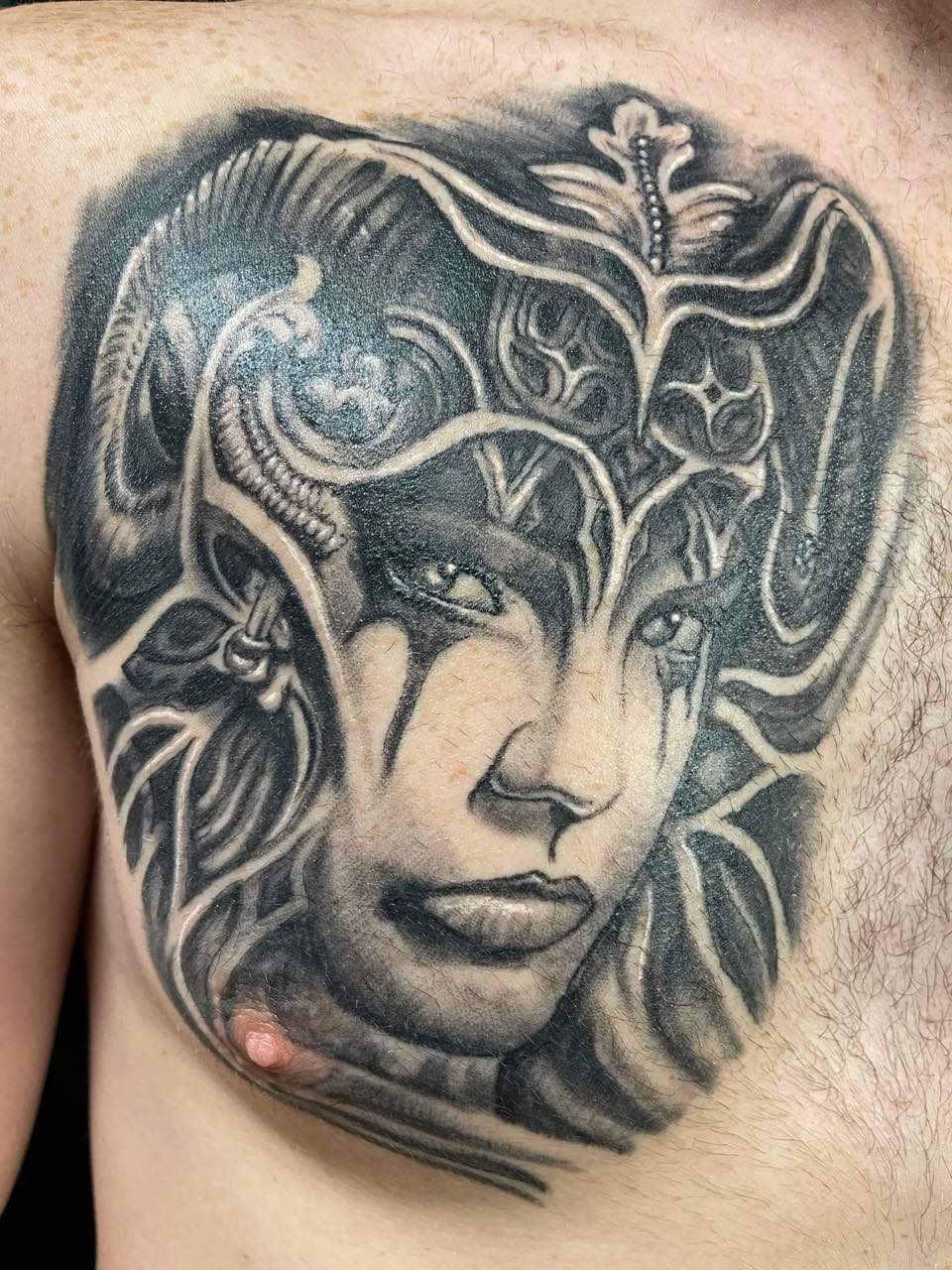 Black and grey fantasy face tattoo with ornate detailing, chest piece