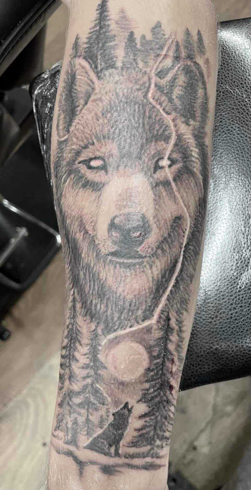 Black and grey wolf head tattoo with forest and moon detail, forearm sleeve